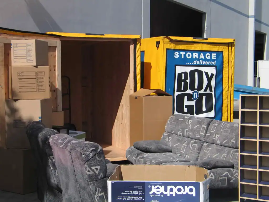 Apartment Movers in Los Angeles CA use Box n Go storage solutions to help with packing and moving. The image shows a portable storage container filled with boxes and furniture, including couches and bookshelves, as part of the moving process.