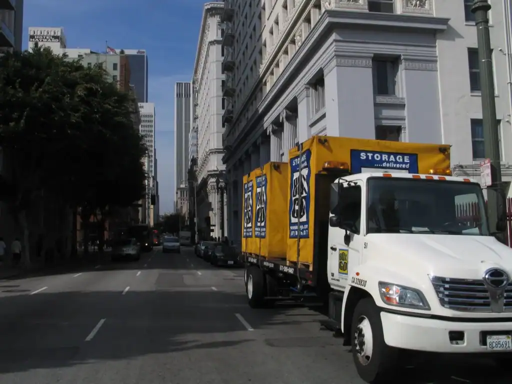 Box-n-Go truck transporting portable moving containers through a busy downtown street, showcasing urban storage and relocation solutions.