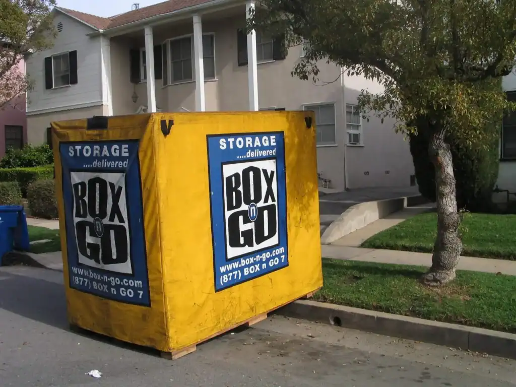 Bright yellow Box-n-Go moving container placed on a residential street in front of a suburban home, offering portable storage and moving solutions.