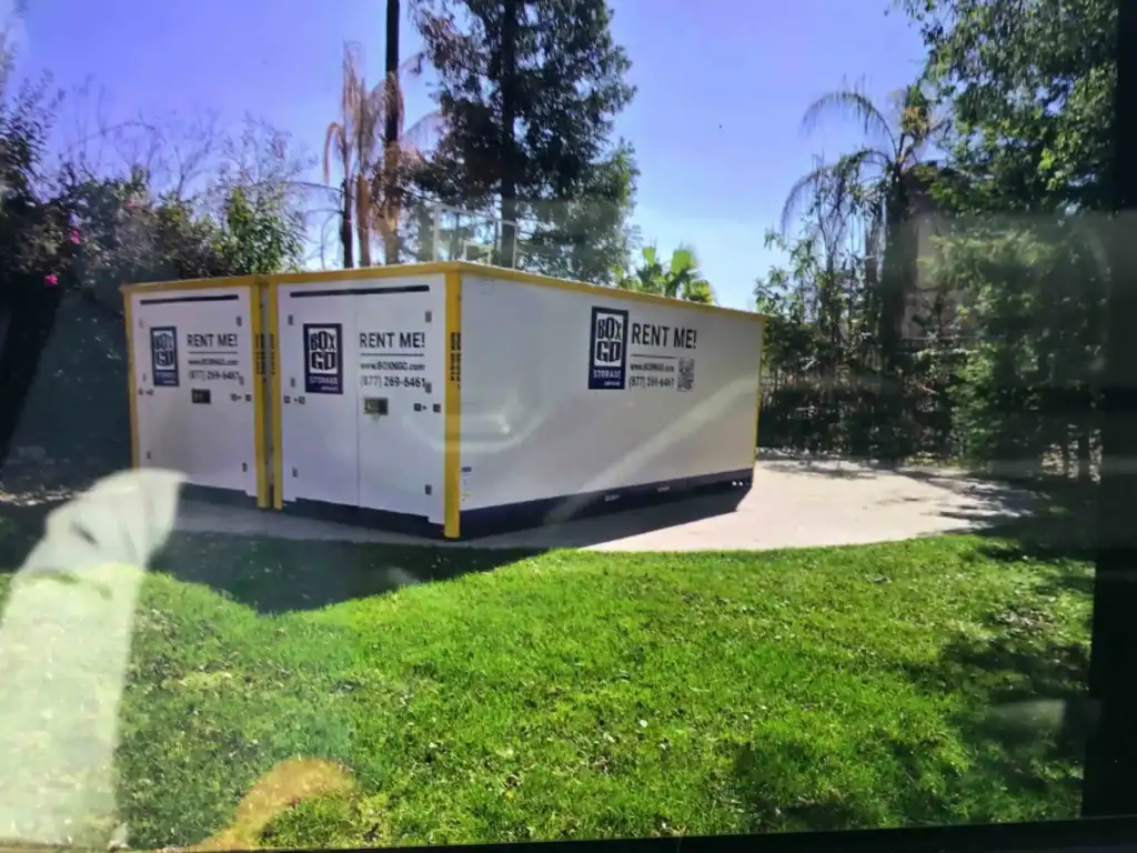 Moving Boxes Delivery in West Hollywood CA - Multiple Box-N-Go portable storage containers are neatly arranged on a concrete pad with green grass in the foreground, ready to facilitate easy moving and storage.