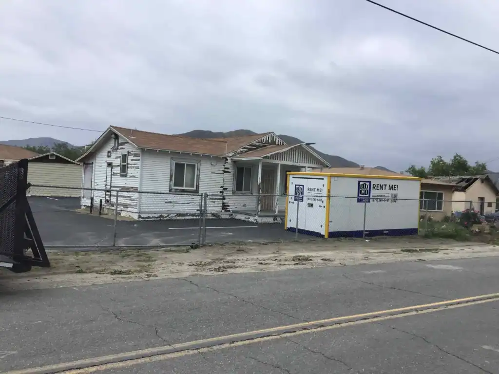 Playa Vista Movers storage container placed in front of an older residential home during relocation service, with mountains in the background and overcast skies.