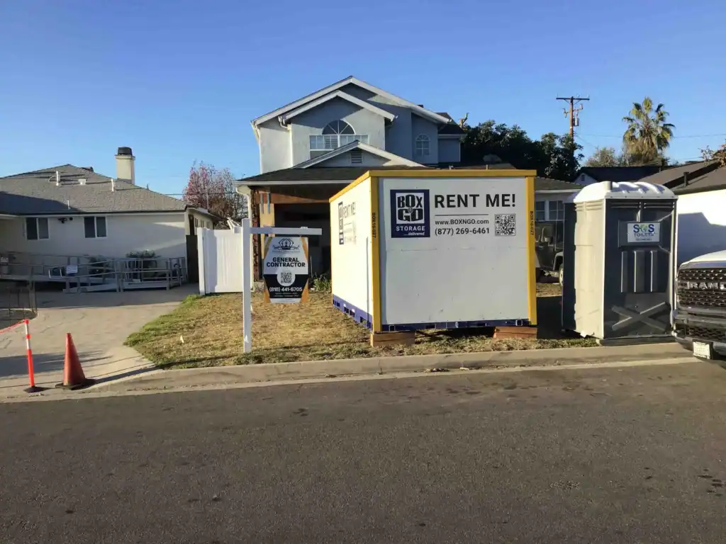 Residential construction site in Santa Monica with a Box-n-Go portable unit used for office inventory storage, featuring a contractor sign and portable restroom on the front lawn.