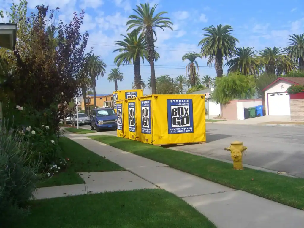 Residential neighborhood with palm trees and Box-n-Go portable containers placed on the street, representing easy and accessible self storage in Paramount CA for local homeowners and renters.
