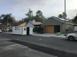 Residential neighborhood with a portable storage unit labeled "Rent Me" placed in front of a house and garage, showing flexible alternatives for people looking to rent a garage for storage or moving needs.
