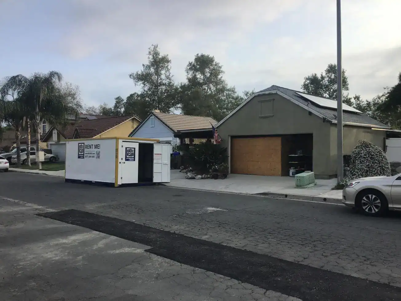 Residential neighborhood with a portable storage unit labeled "Rent Me" placed in front of a house and garage, showing flexible alternatives for people looking to rent a garage for storage or moving needs.