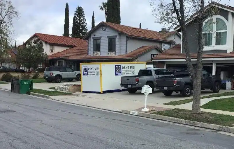 A residential neighborhood in Sherman Oaks featuring a portable storage container rental placed in a driveway for home renovation or moving purposes, with trucks parked nearby and suburban homes in the background.
