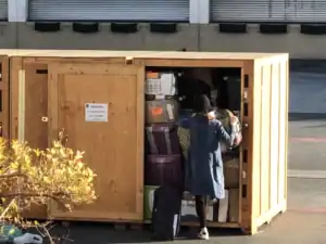A woman carefully packing fragile items for storage inside a large wooden container, surrounded by boxes, bins, and luggage for safe transport and organization.