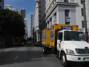 Box-n-Go truck delivering portable storage containers in downtown city streets, offering reliable moving and storage services for homes, students, and businesses.