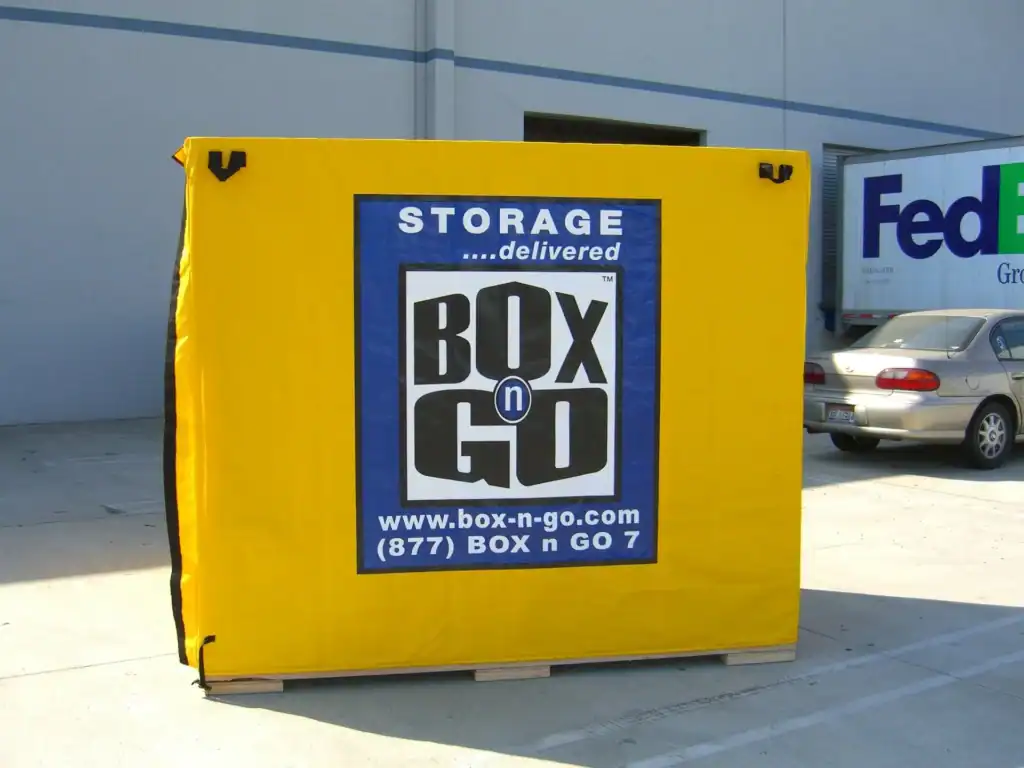 Bright yellow portable storage container from Box-n-Go, a leading choice among affordable local moving companies, placed outside a warehouse facility next to a FedEx truck and parked car.