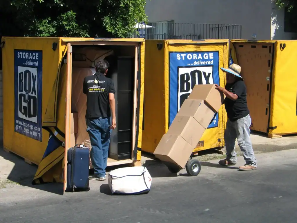 Workers packing fragile items for storage into portable storage containers, carefully loading labeled moving boxes and household belongings to ensure safe transport and protection of delicate items.