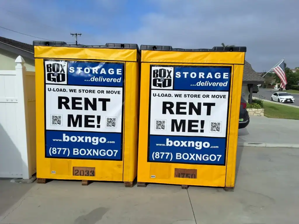 Yellow Box-n-Go portable storage containers with signage promoting moving and storage services, featuring the message “Rent Me,” website link, and contact number for convenient self-storage and moving solutions.