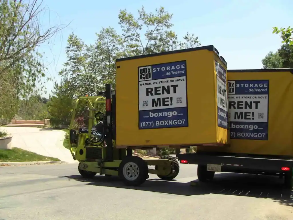 Forklift loading a yellow Box-n-Go storage container onto a truck in a residential neighborhood, showcasing convenient portable storage Reseda solutions for moving and on-site storage.