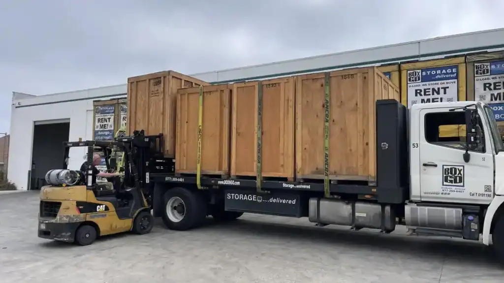 Forklift loading wooden portable storage Montrose units onto a Box-n-Go delivery truck at a storage facility, showing secure and efficient mobile storage transport services.