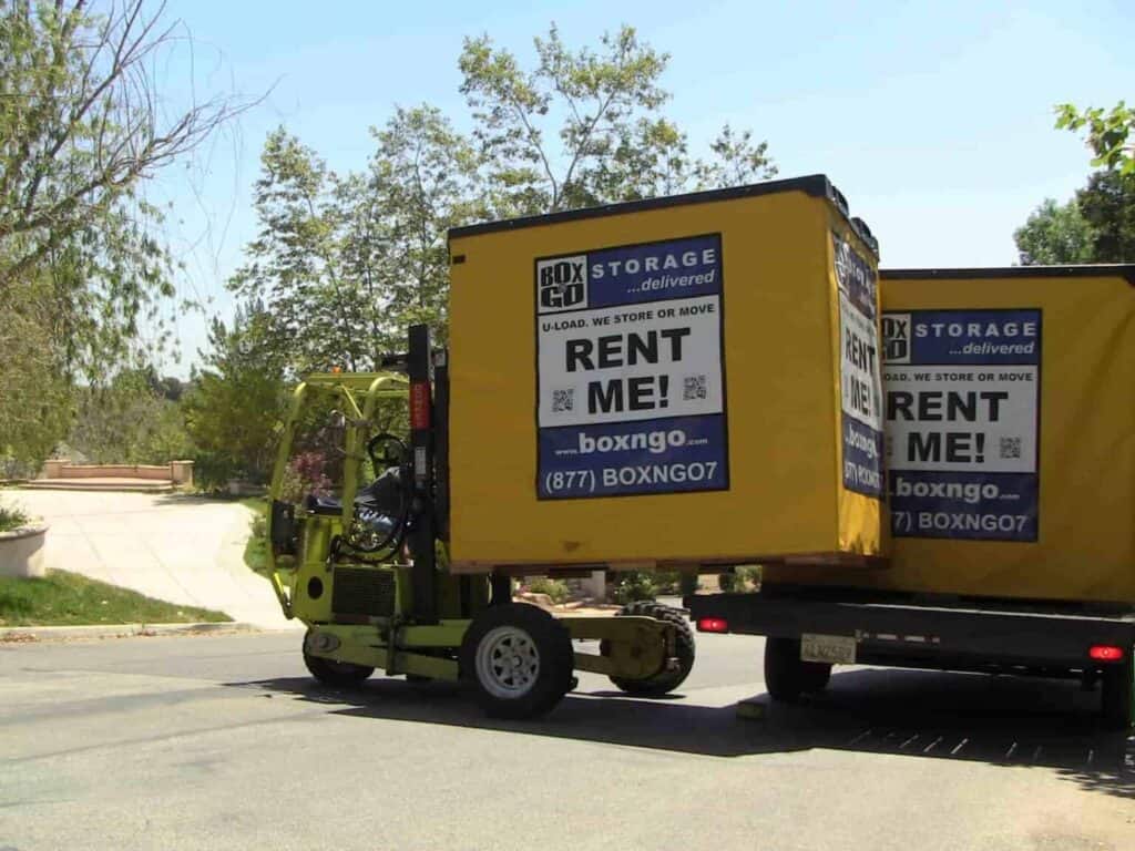 Forklift unloading a Box-n-Go portable self storage container from a delivery truck in a residential neighborhood, illustrating convenient on-site portable self storage solutions.