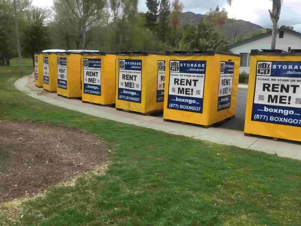Multiple bright yellow portable storage units from Box-n-Go lined up in a park setting, showcasing convenient portable storage Montrose options for easy moving and temporary on-site storage.