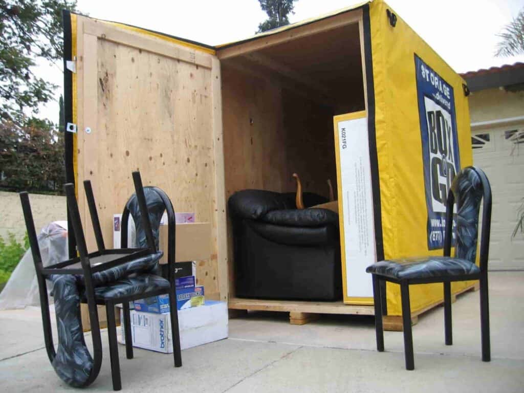 Open portable storage rental unit on a driveway filled with household furniture, boxes, and chairs, showing how conveniently items can be packed and stored for moving or temporary storage.