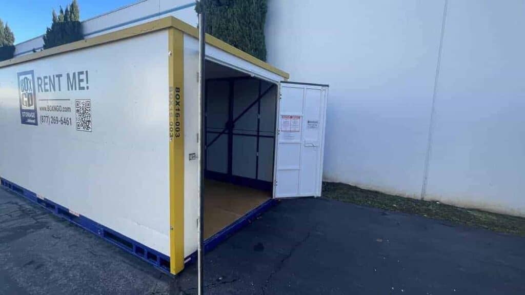 Outdoor portable storage box provided by a portable storage box company, showing an open rental storage container ready for loading beside a commercial building.
