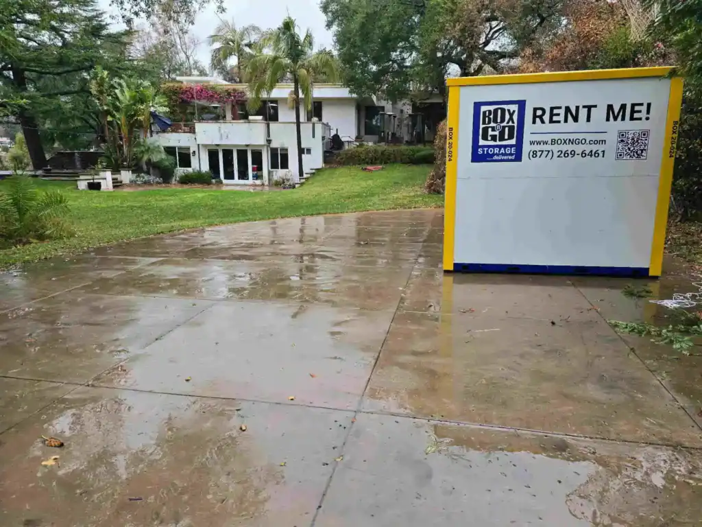 Portable storage Reseda container placed on a wet residential driveway in front of a modern home, showing a Box-n-Go storage unit used for convenient moving and on-site storage solutions.