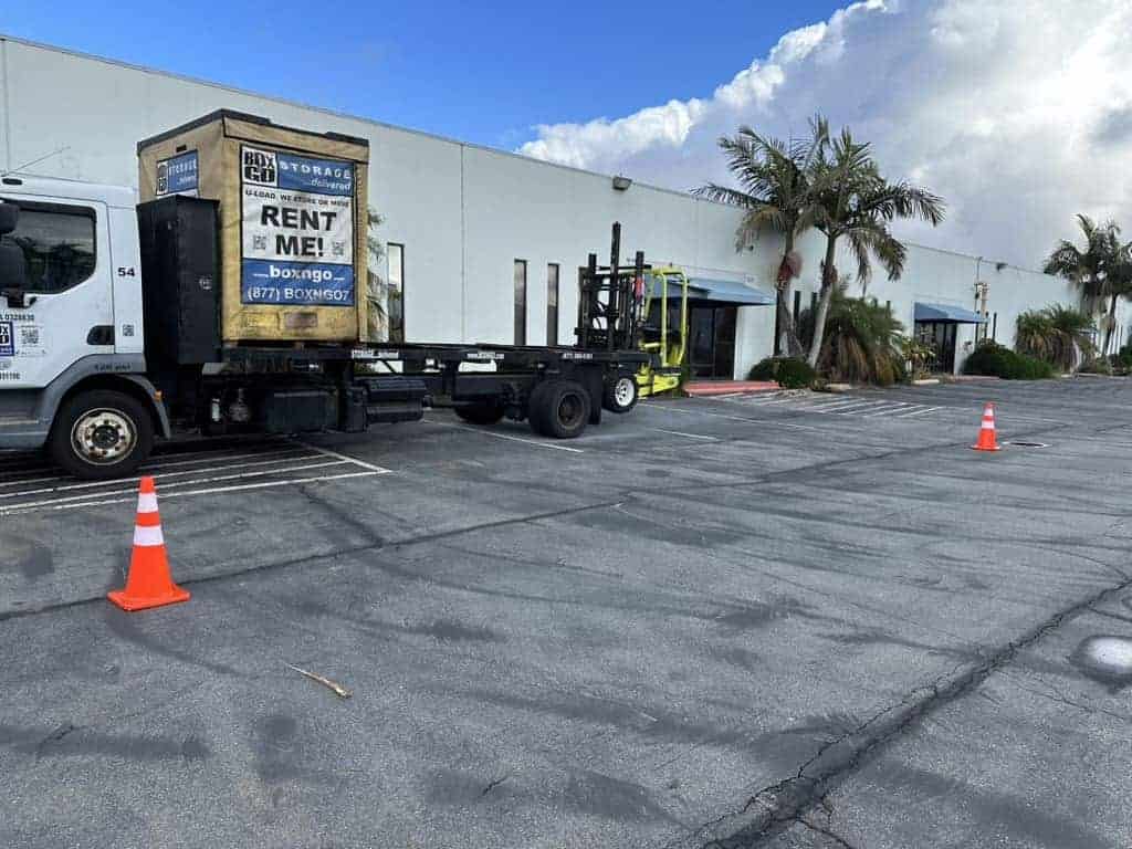 Truck delivering a Box-n-Go unit in a commercial parking lot, illustrating the convenience of finding portable storage near me for moving, business storage, and on-site delivery needs.