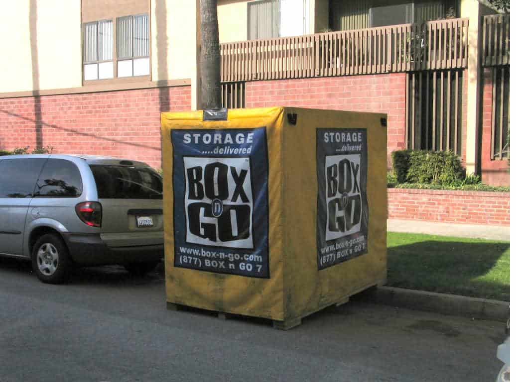 A storage unit student discount unit parked in a street with brick building visible.
