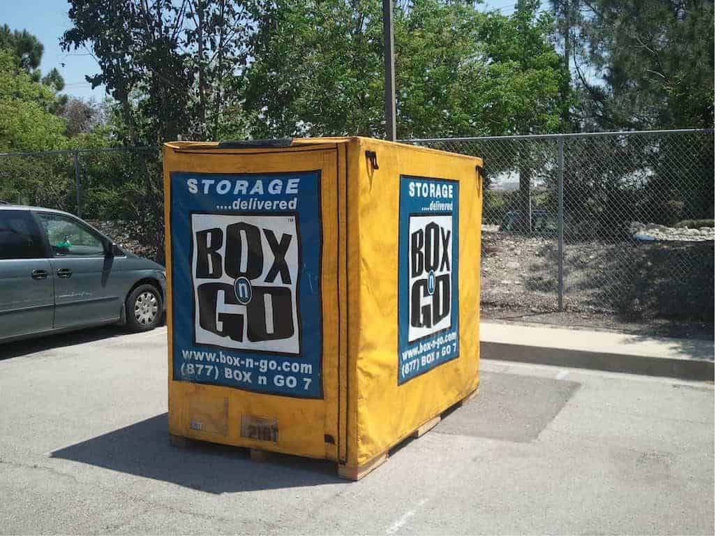 Yellow Box-n-Go student storage units in a parking lot near a chain-link fence.