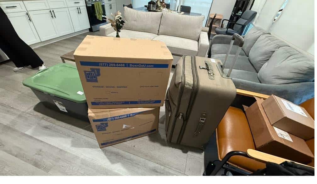 Student items including boxes and a gray suitcase packed and labeled for usc storage.
