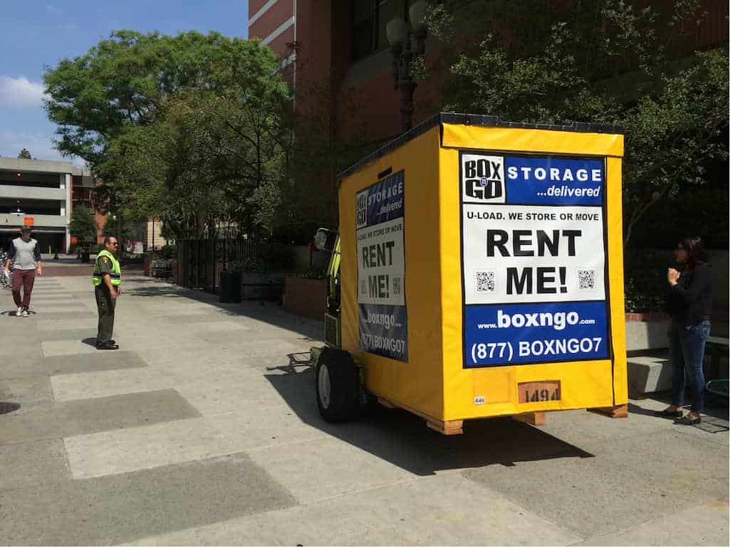 Portable lmu summer storage unit next to parking garage on a sunny day.