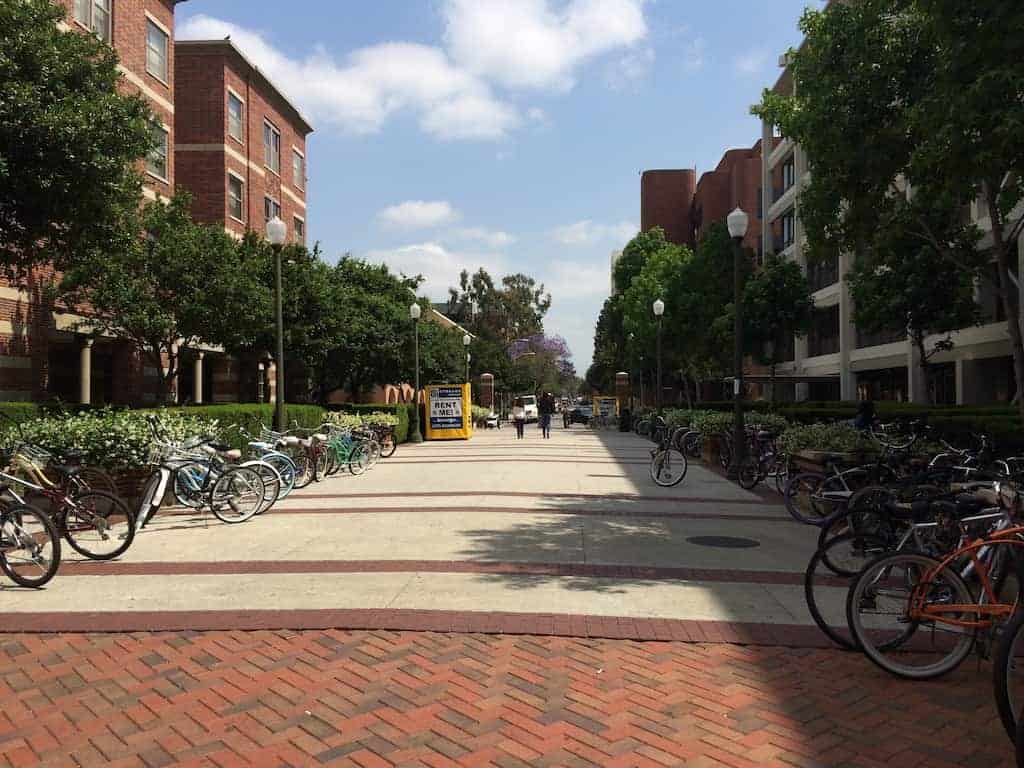 A wide brick walkway with bicycles racked along both sides and a container standing at the far end, placed for CalArts student storage.