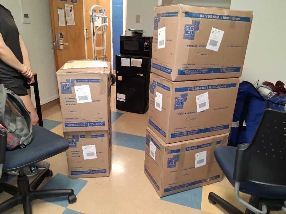 Labeled cartons, a black microwave and a desk chair waiting in a residence hallway on Orange Coast College move out storage day.
